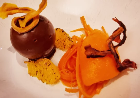 Sphère en chocolat avec un crémeux de carottes, accompagnée de son sorbet aus agrumes, ses carottes en pickles et ses quartiers d'orange brulés.