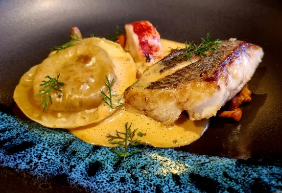 Dorade royale pêchée à la ligne, juste saisie avec une queue de homard accompagnée des pinces en raviole, d'une tombée de girolles et d'une sauce au vin jaune.