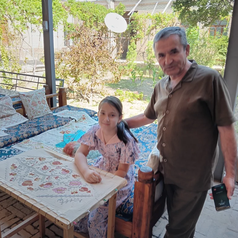 A Gijduvan, Farzona, 8 ans, la petite-fille du maître céramiste Abdullo Narzullaevs s'essaie à la broderie au crochet, sous l’œil complice de son grand-père. Photo Claude Vautrin