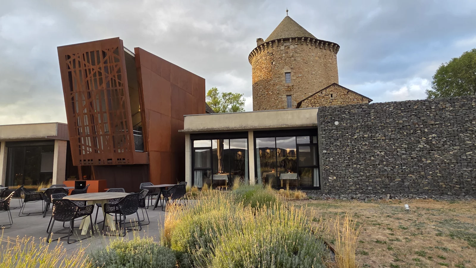 En contrebas de la tour du château du Couffour, le restaurant Serge Vieira est un bâtiment contemporain construit en pierre de lave, en acier corten et en verre.
