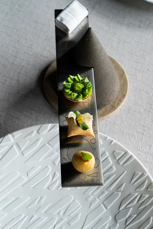 Les amuse-bouches et les mignardises sont servis sur une réglette en acier, taillée par un coutelier de Thiers. La réglette se glisse astucieusement dans le cône en pierre de lave de Volvic représentant un volcan d'Auvergne.